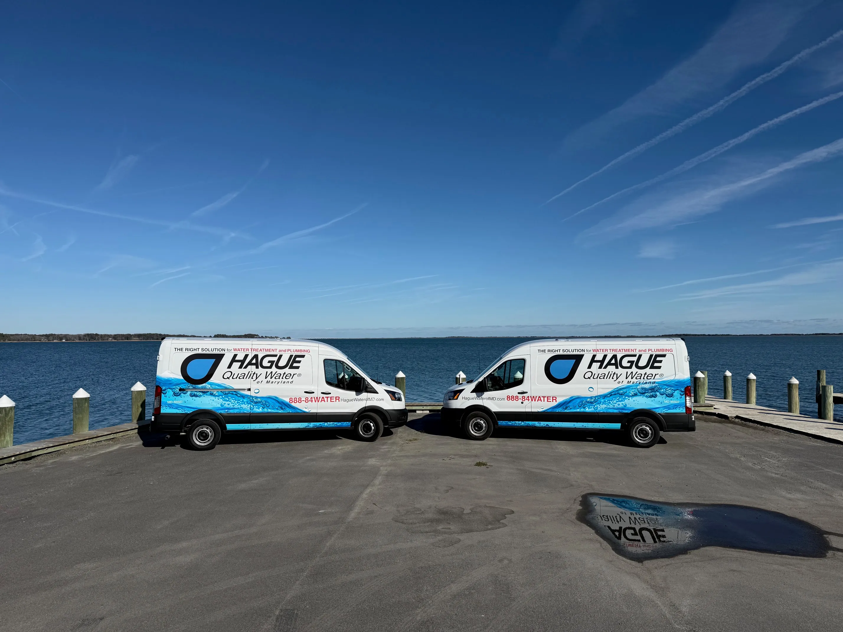 Two branded Hague Quality Water of Maryland vans parked on a Chesapeake Bay dock